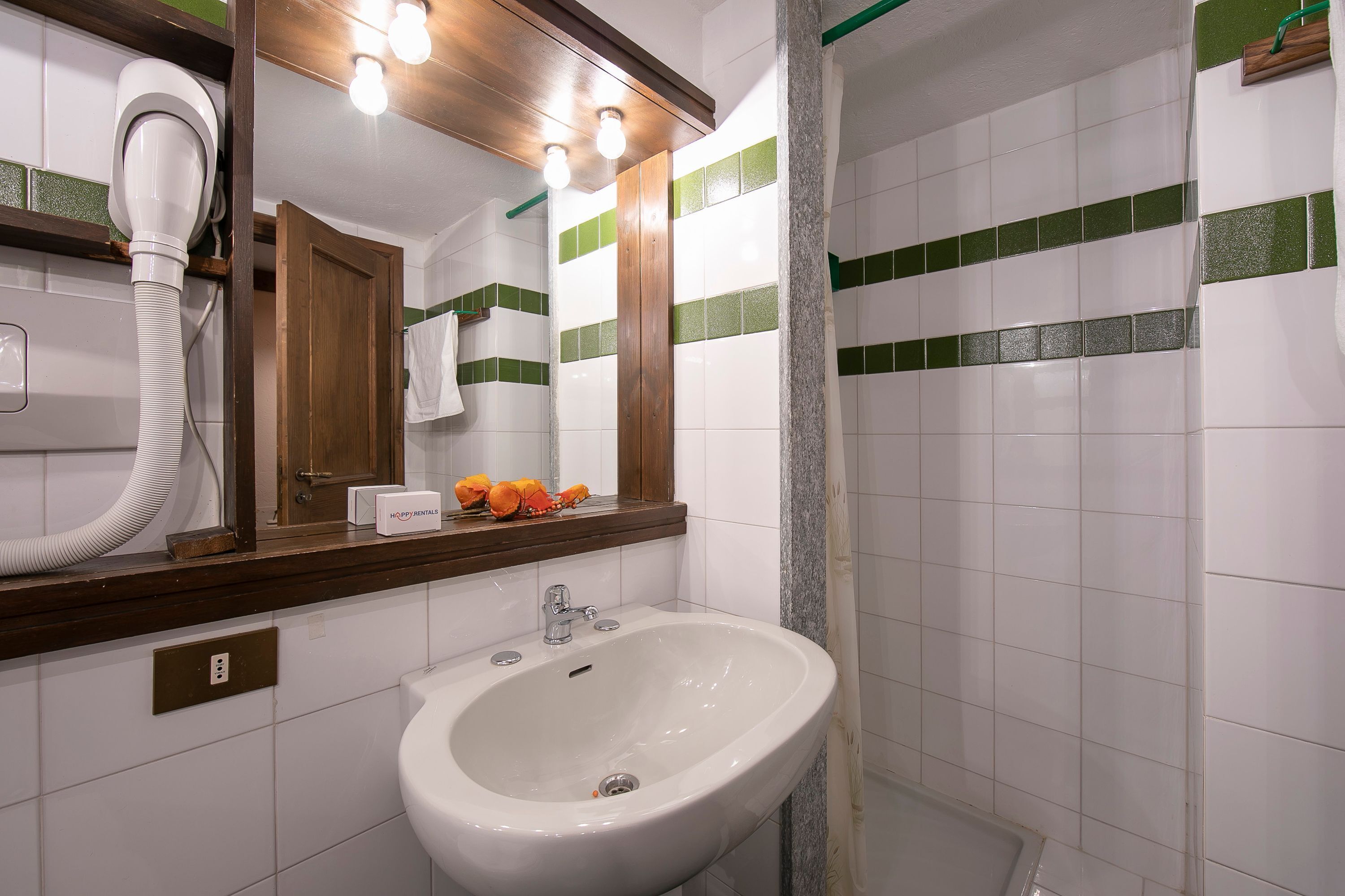 Un bagno con un lavandino bianco, uno specchio e un asciugacapelli.