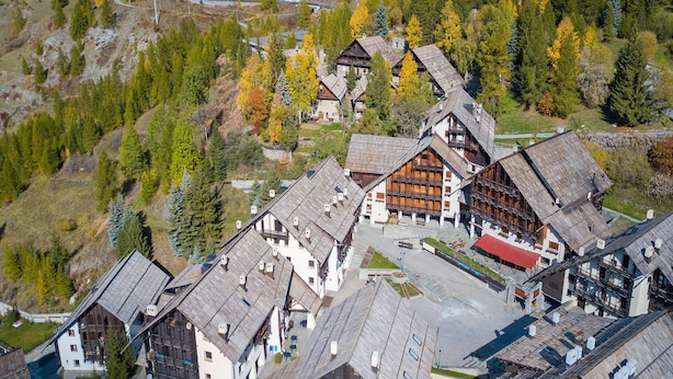 Il s’agit d’un bâtiment traditionnel de style chalet, en bois, doté d’un toit à forte pente et entouré d’une zone boisée aux couleurs automnales.