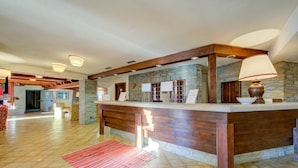 Un hall d’entrée spacieux avec un mur en pierre, un comptoir d’accueil en bois et un tapis rouge.