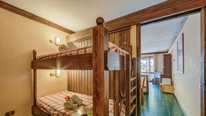 Ein Etagenbett mit karierter Bettdecke und Holz-Kopfstütze. Darüber ist eine Wandleuchte angebracht.