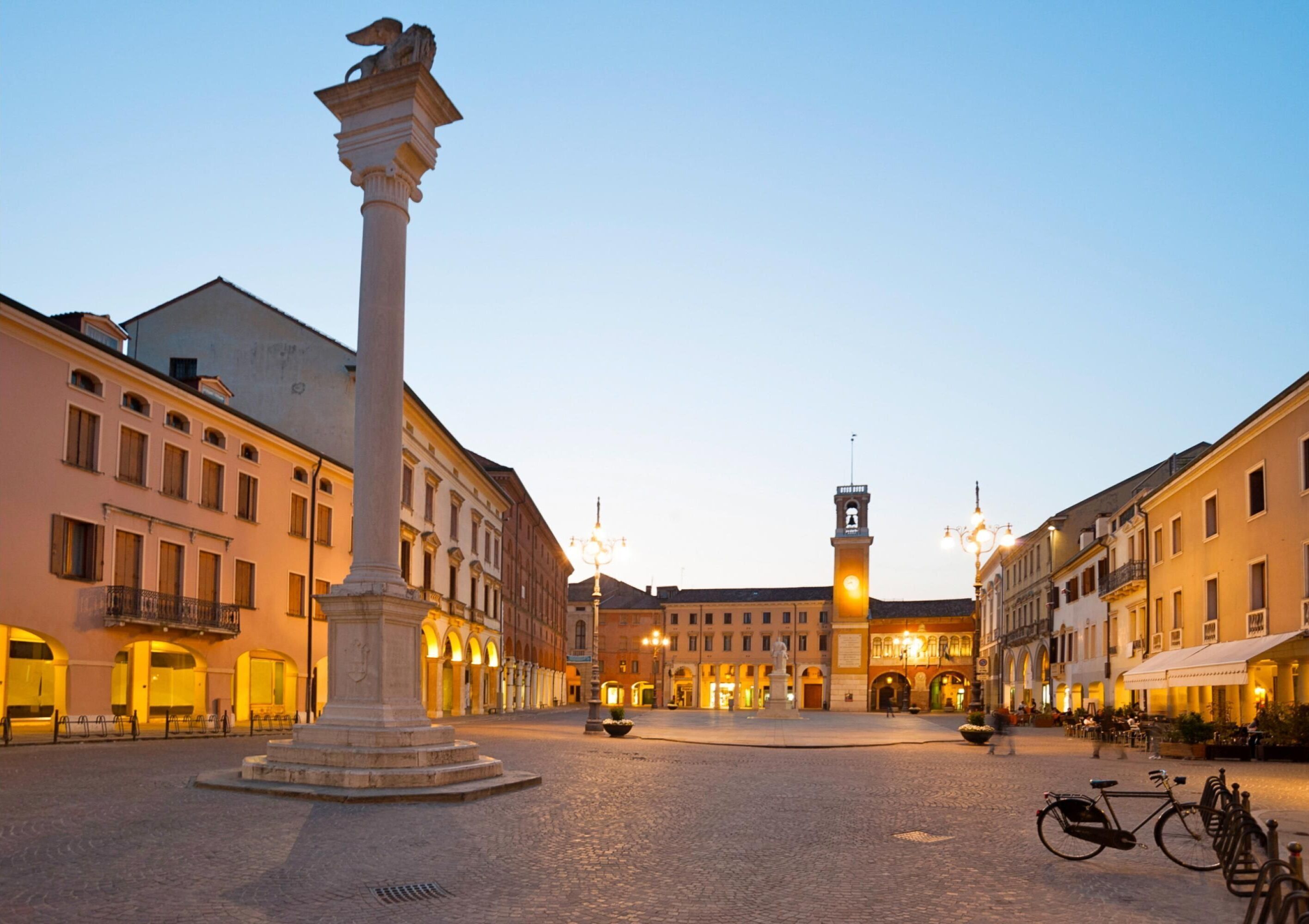 A historic square with a central monument, cobblestone pavement, and surrounding classical buildings.