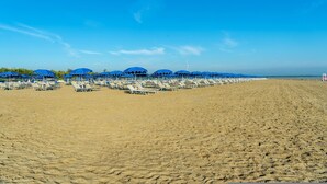 A beach with rows of blue umbrellas and white lounge chairs. - Albarella Maisonette S3M 2 (Rosolina)