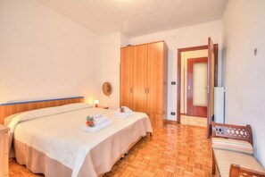 Un dormitorio con cama, armario, mesita de noche y un pequeño rincón de descanso.