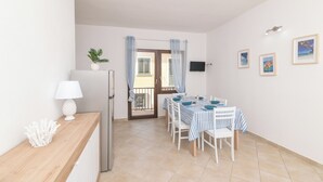 A dining area with a table set for four, white chairs, a striped tablecloth, and a white lamp on a wooden sideboard. - Appartamento Rosmarino In The City Center (Santa Teresa di Gallura)