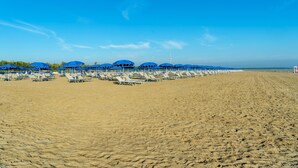Una spiaggia con file di lettini e ombrelloni sotto un cielo azzurro.