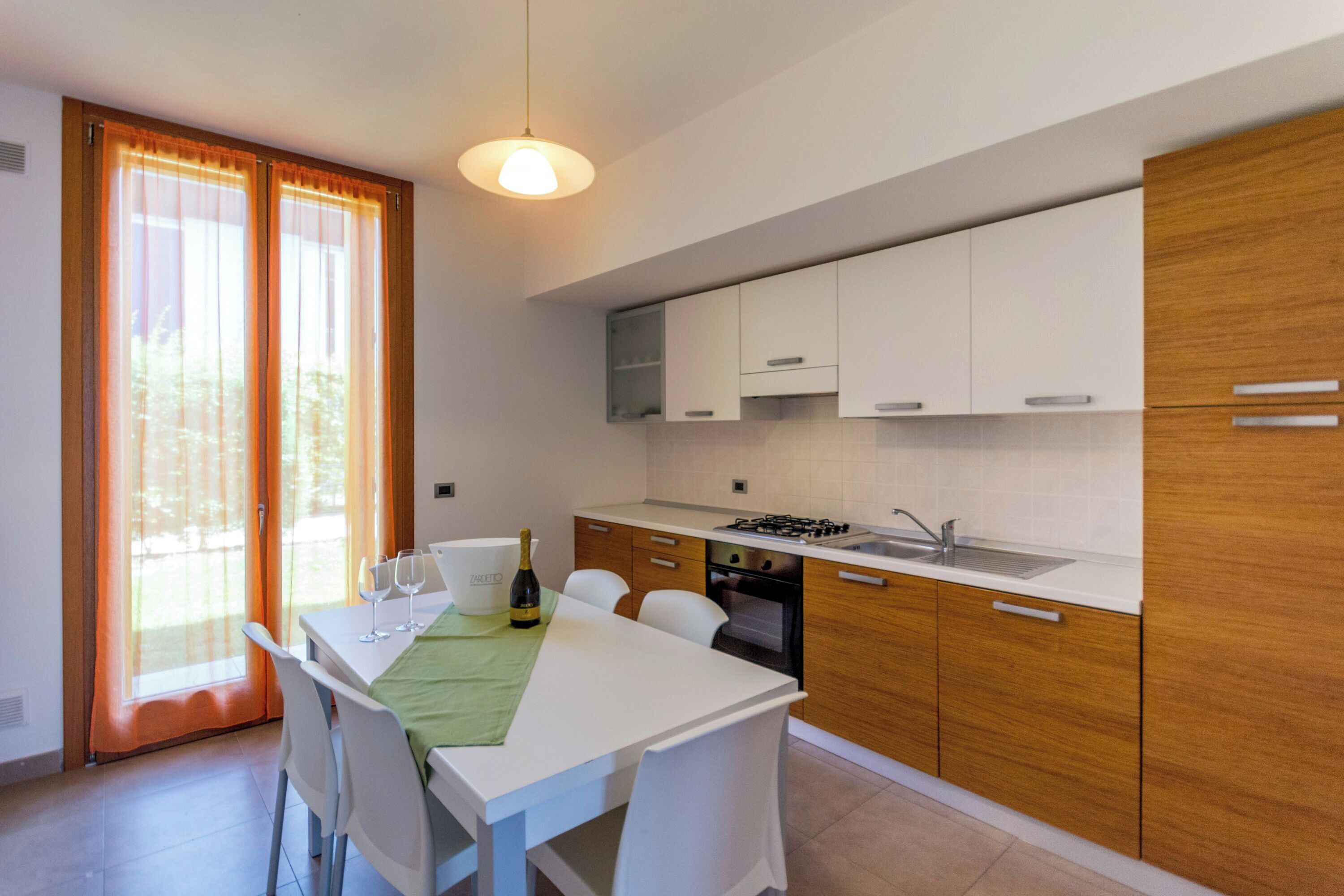 A modern kitchen with white cabinets, a dining table with chairs, and a bottle of wine.