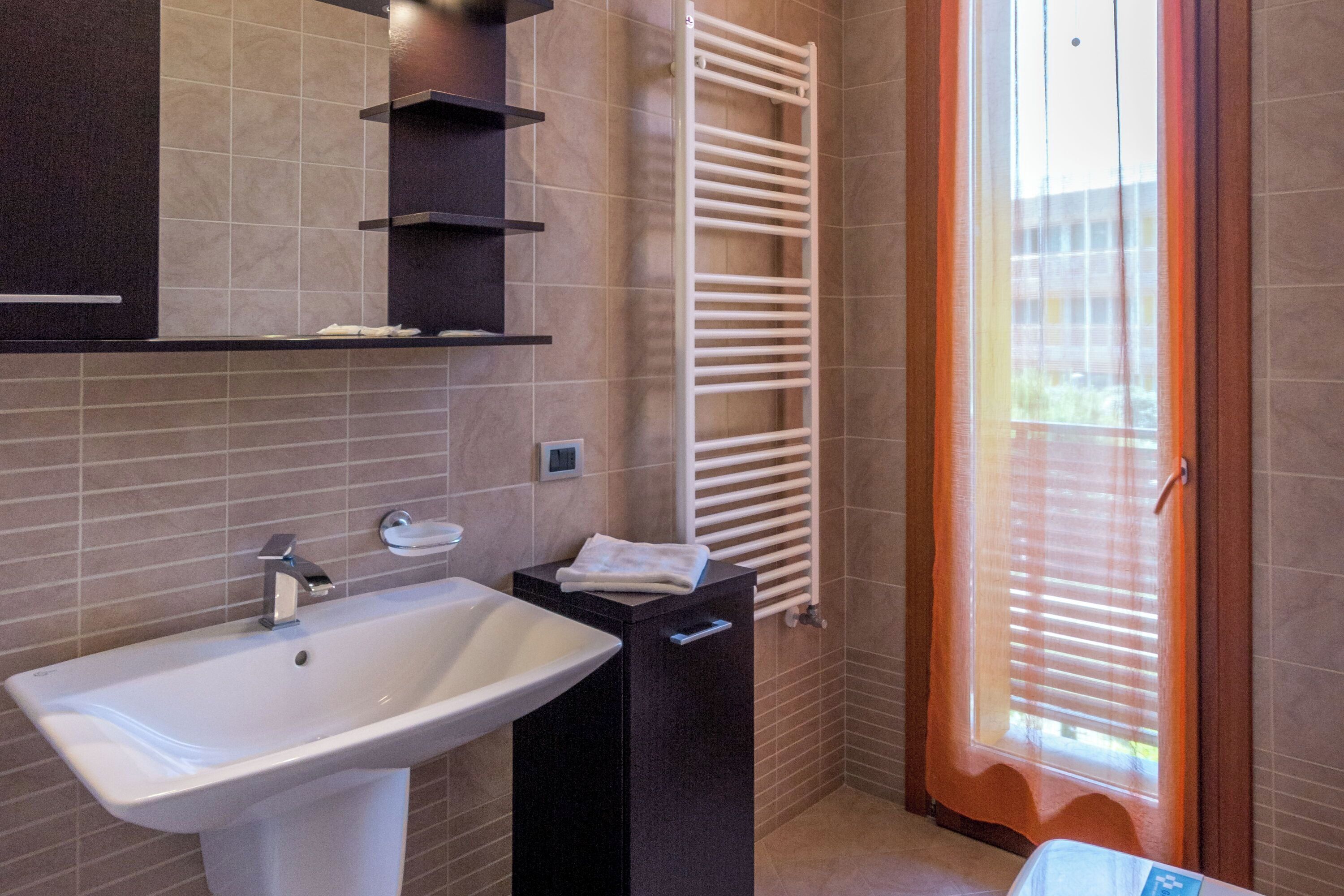 Une salle de bain avec un lavabo blanc, un porte-serviettes et une fenêtre avec des stores.