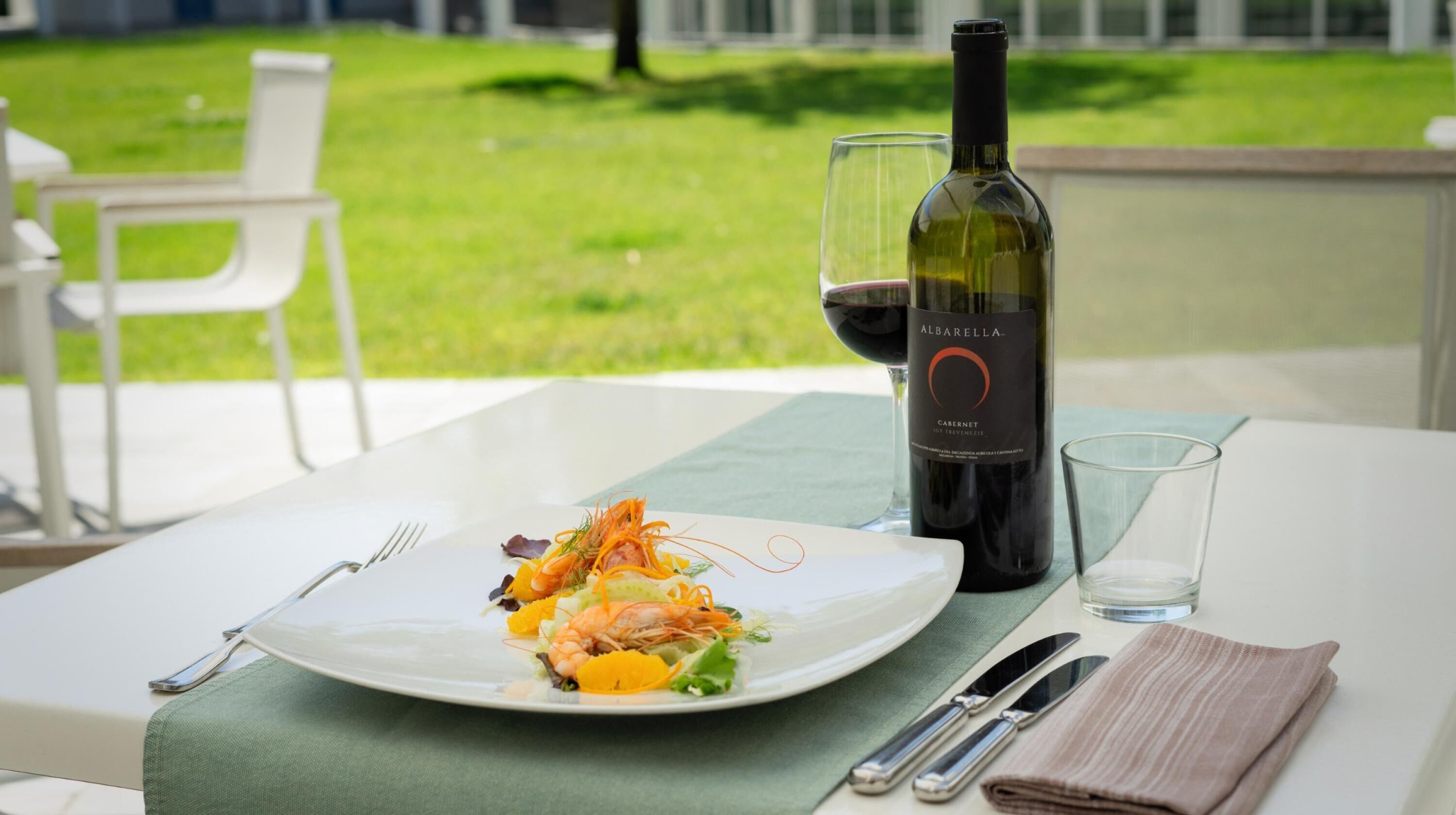 A dining table with a plate of food, a wine bottle, and a glass of wine.