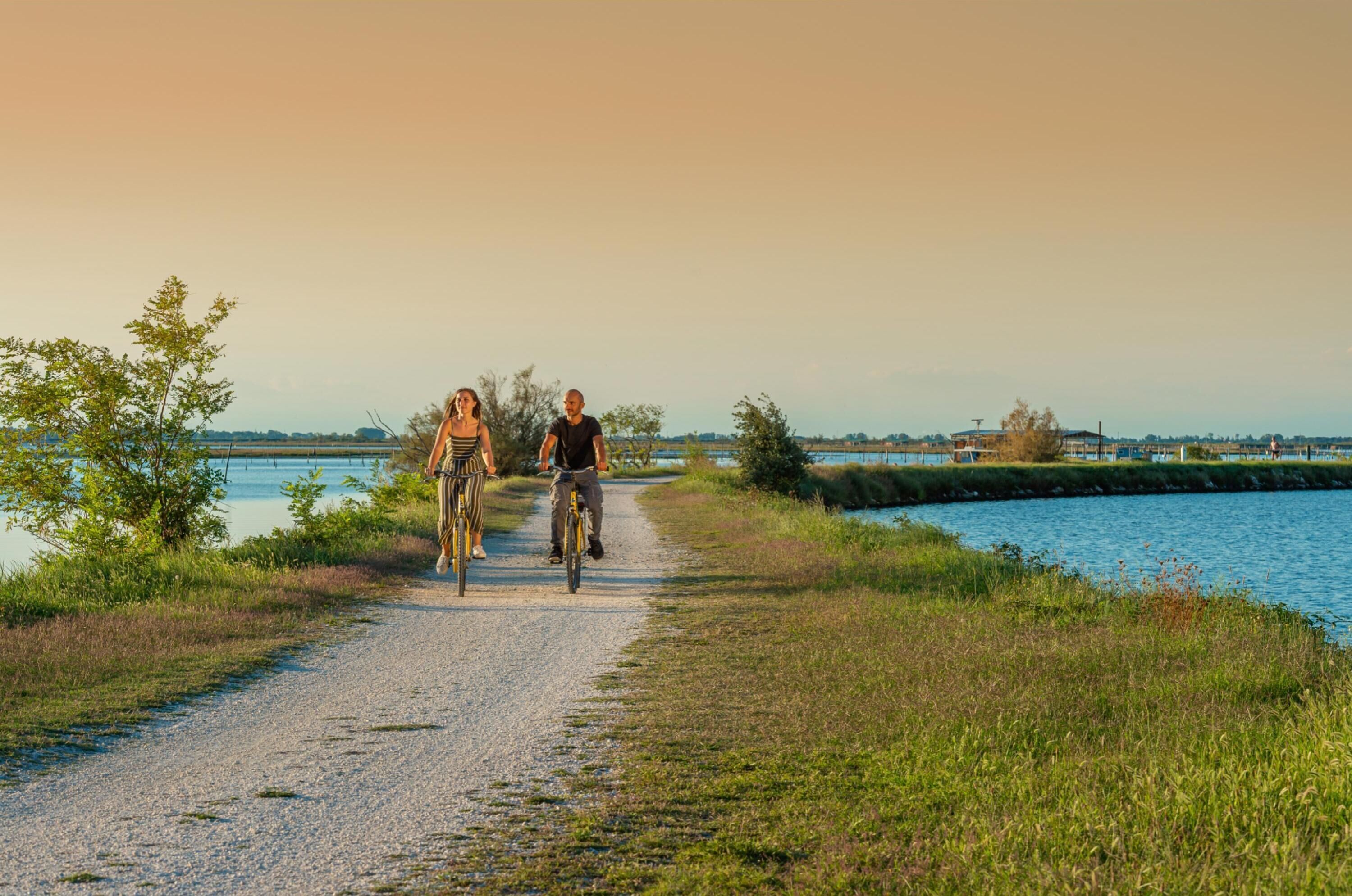 Twee personen fietsen op een grindpad langs het water.