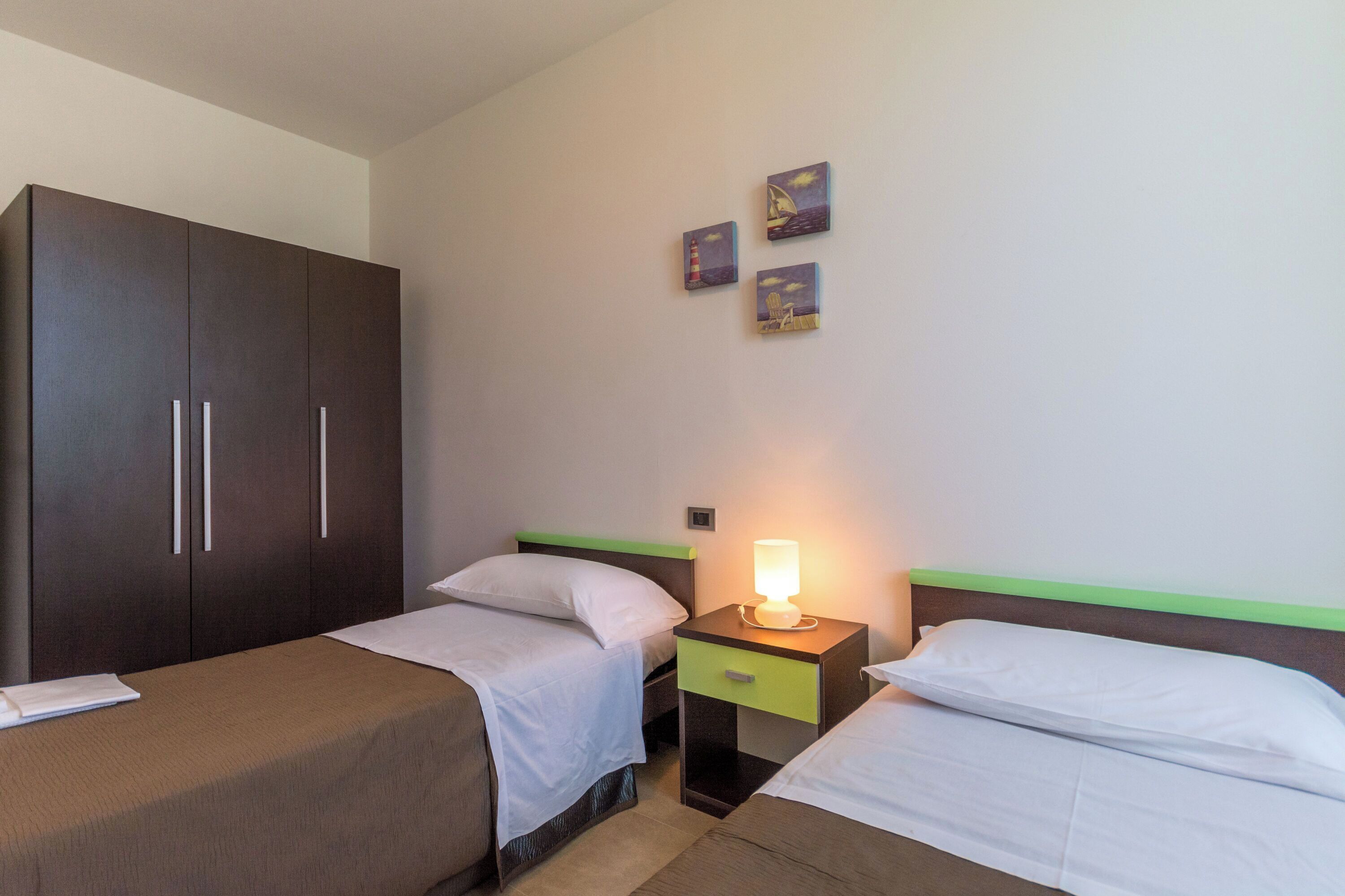 Habitación de hotel con dos camas individuales, un armario, una mesita de noche con lámpara y tres obras de arte en la pared.