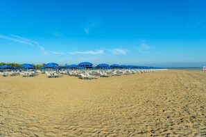 A beach with rows of sunbeds and umbrellas under a clear blue sky. - Albarella Maisonette S3M 3 (Rosolina)