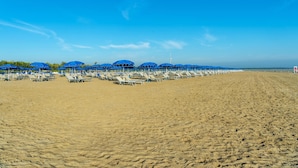 A beach with rows of sunbeds and umbrellas under a clear blue sky. - Albarella S3 2 in Isola Albarella (Rosolina)