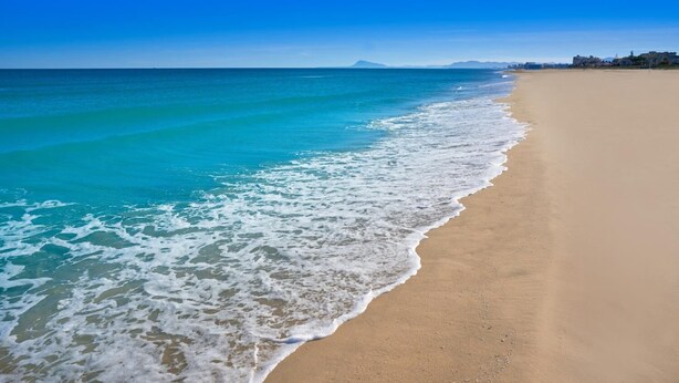 Une plage aux eaux turquoise et limpides, bordée d’un rivage sablonneux.