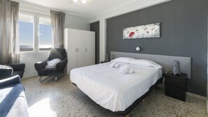 Une chambre d’hôtel comprenant un lit, une chaise, une armoire, une table de chevet et un ventilateur de plafond.