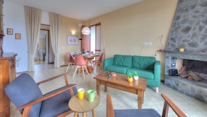 A living room with a green sofa, wooden coffee table, and chairs. There is a dining area with a table and chairs in the background. - La Perla Bianca Lake View (Massino Visconti)