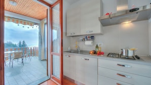 A kitchen with a view to a balcony, a stove, and various kitchen items. - La Perla Bianca Lake View (Massino Visconti)