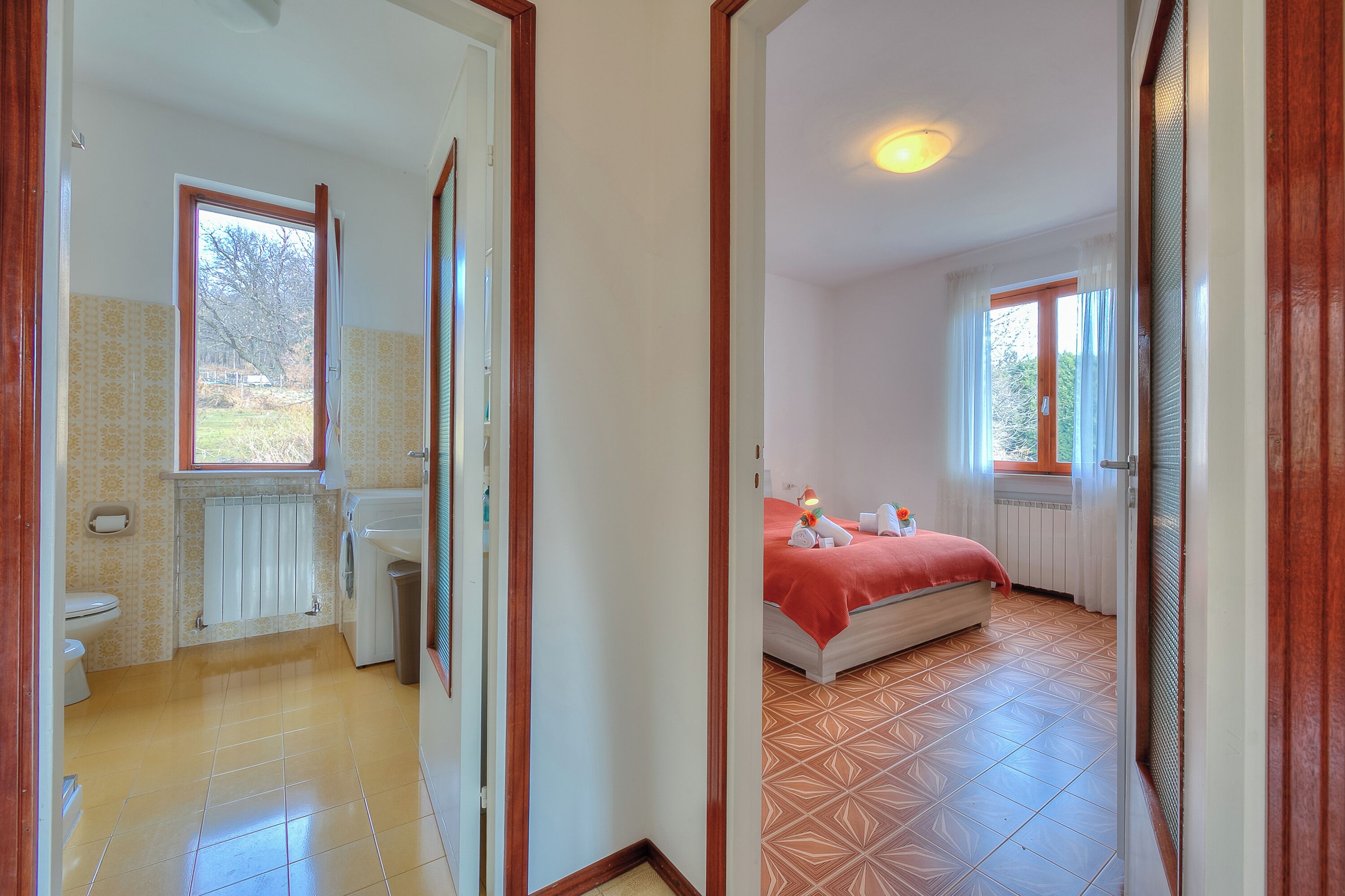 A hotel room with a bathroom, a bed with a red blanket, and a window.