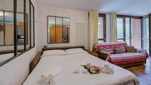 A hotel room with a large bed, a sofa, a mirror, and a window with curtains.