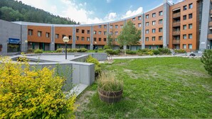 A modern building with multiple floors, a courtyard with grass and plants, and a mountain backdrop.