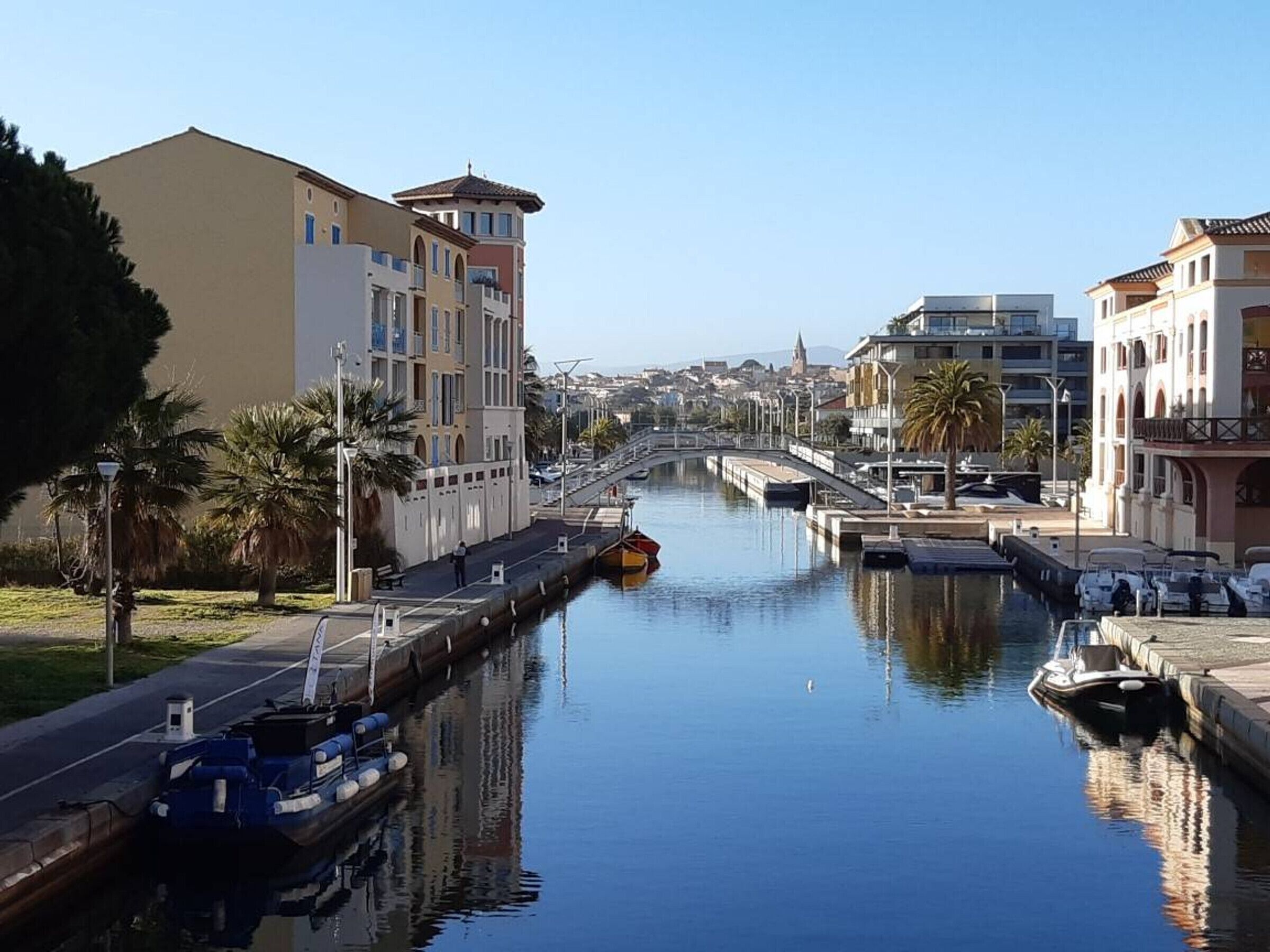 A canal with boats docked, a bridge, and buildings along the water.