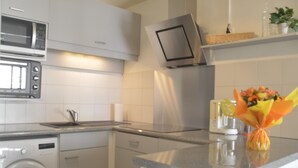 Una cocina moderna con microondas, horno y lavadora. Hay una cesta sobre la encimera y un jarrón con flores.