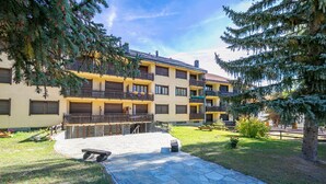 A multi-story building with balconies, a stone pathway, and surrounding greenery. - Il Nido di Elda few Steps From Skiing (Bardonecchia)