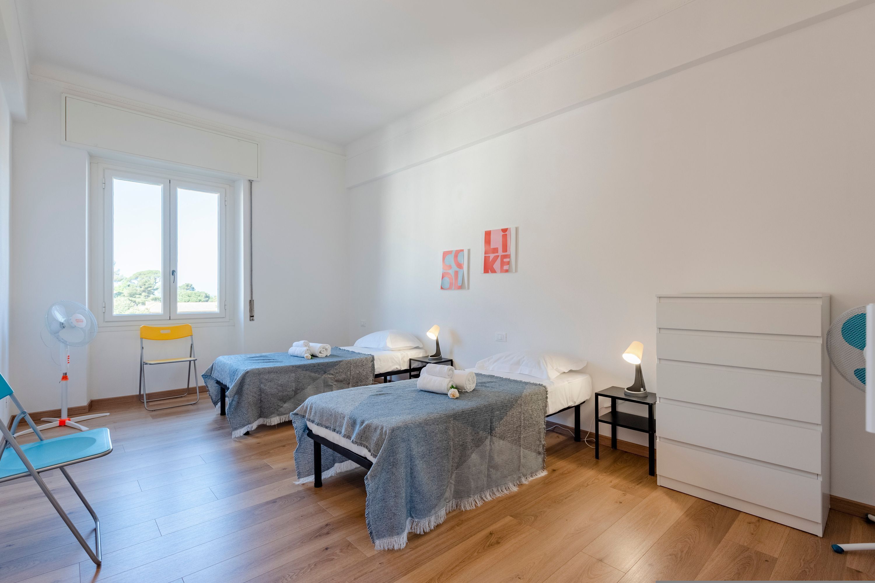 A room with two beds, a chair, a desk, and a window.