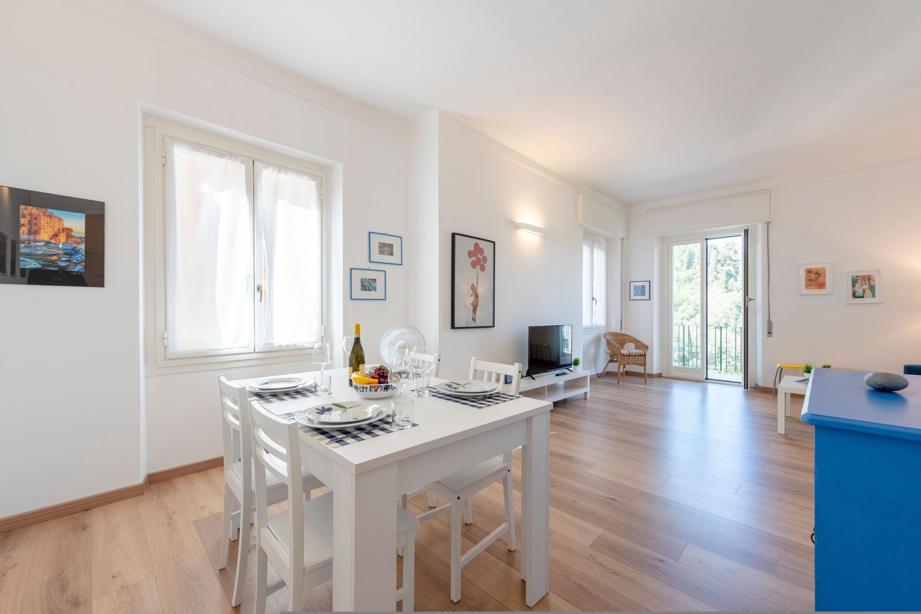 A modern, well-lit dining area with a white table set for four, a television, and a blue cabinet.