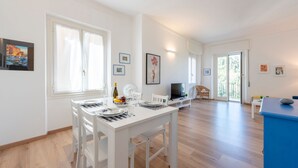 A modern, well-lit dining area with a white table set for four, a television, and a blue cabinet. - Central Flat in Camogli (Camogli)