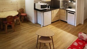 A compact kitchen with white appliances, a dining area with a wooden table and chairs, and a small kitchenette. - Renovated large studio for 4, center station, ski-in/ski-out (Les Orres)