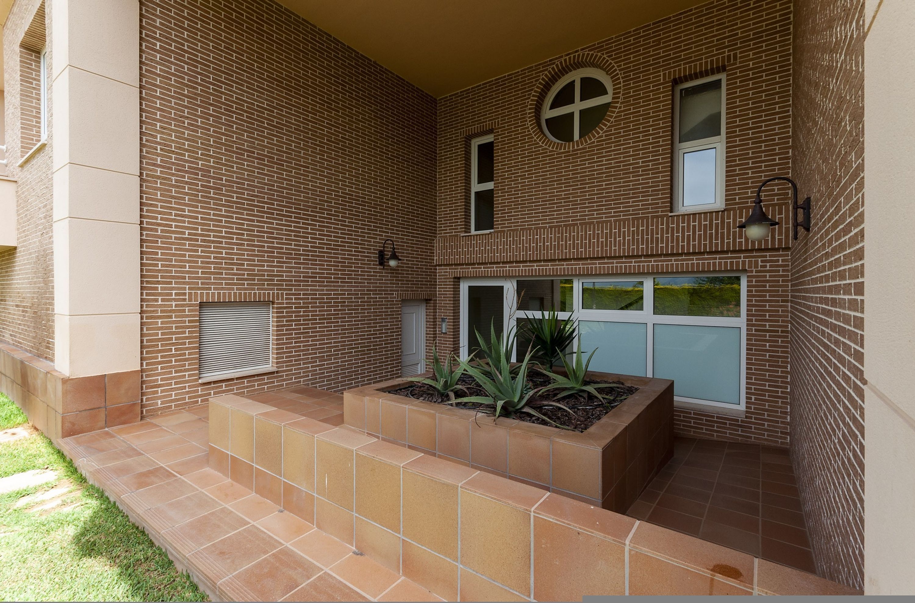 Un bâtiment moderne avec une façade en briques, un petit jardin agrémenté de plantes et une fenêtre donnant sur un espace verdoyant.