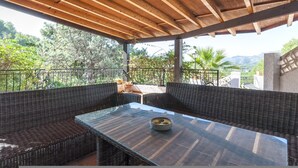 An outdoor patio with wicker furniture and a glass table, overlooking a scenic landscape with trees and mountains. - Casabra in Ador With 5 Bedrooms and 3 Bathrooms (Palma de Gandia)