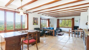 A spacious living area with a wooden ceiling, large windows offering a view of the countryside, a dining table with chairs, and a sofa. - Casabra in Ador With 5 Bedrooms and 3 Bathrooms (Palma de Gandia)