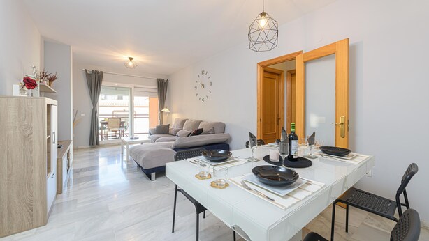 A modern dining area with a white table set for four, a wooden door, and a view of a balcony with a sofa. - La Casa De Bebita in Fuengirola (Fuengirola)