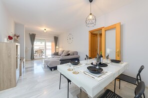A modern dining area with a white table set for four, a wooden door, and a view of a balcony with a sofa. - La Casa De Bebita in Fuengirola (Fuengirola)