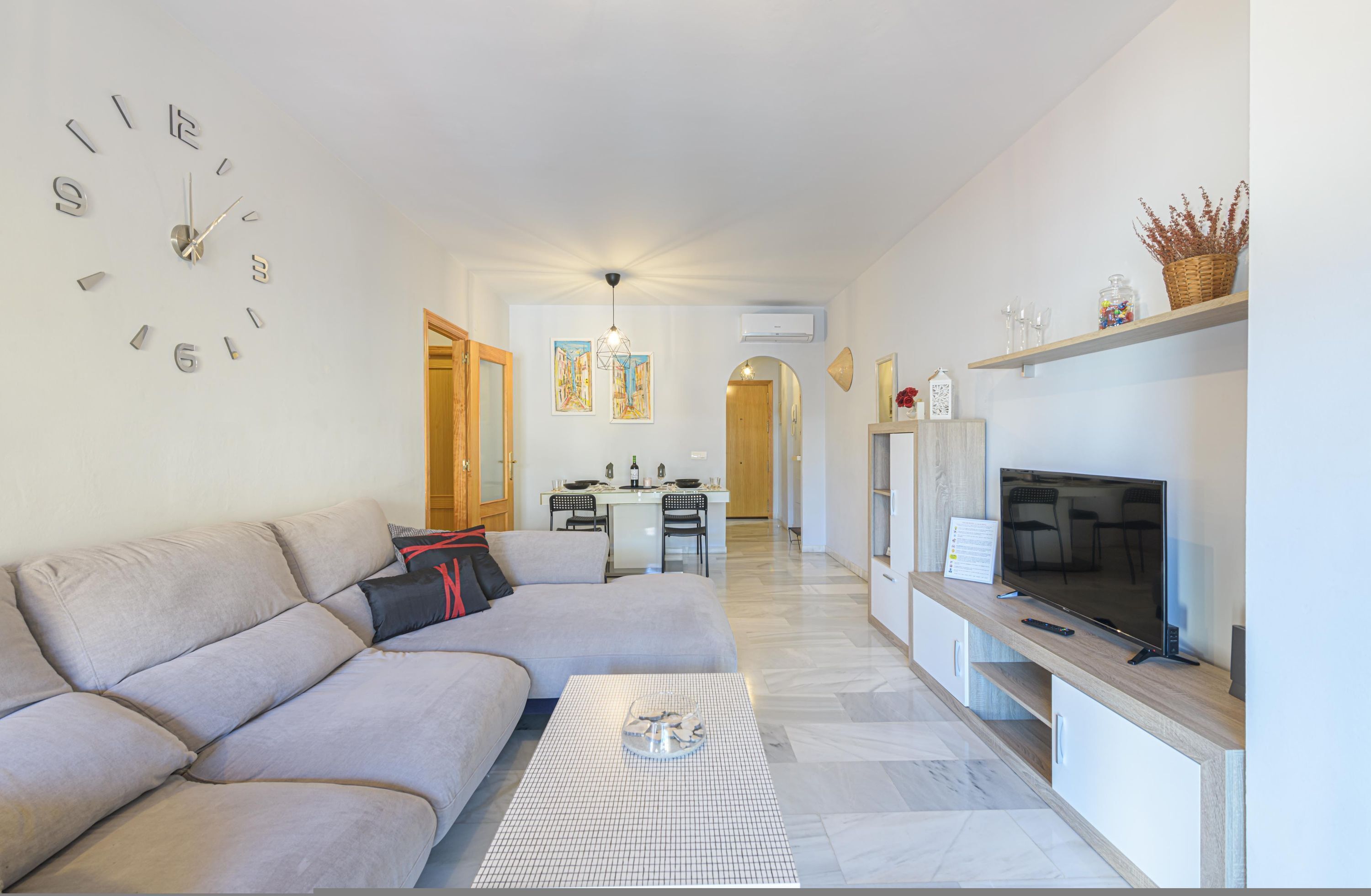 A modern living room with a sofa, a coffee table, a TV, and a dining area in the background.