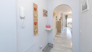 A hallway with a white wall, a telephone, a decorative heart garland, a small shelf with a pink bag, and a doorway leading to another room. - La Casa De Bebita in Fuengirola (Fuengirola)