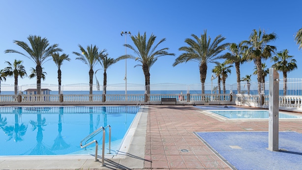 A swimming pool with a tiled deck, palm trees, and a clear blue sky. - Algarrobo Costa in Algarrobo-costa (Algarrobo)