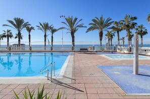 A swimming pool with a tiled deck, palm trees, and a clear blue sky. - Algarrobo Costa in Algarrobo-costa (Algarrobo)