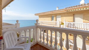 A balcony with white railings, a white chair, and a view of the sea and a building with a tiled roof. - El Morche in El Morche (Torrox)
