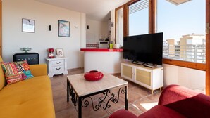 A living room with a sofa, a TV, a small table, and a kitchen area with a red counter. - La Caracola in Torremolinos (Torremolinos)