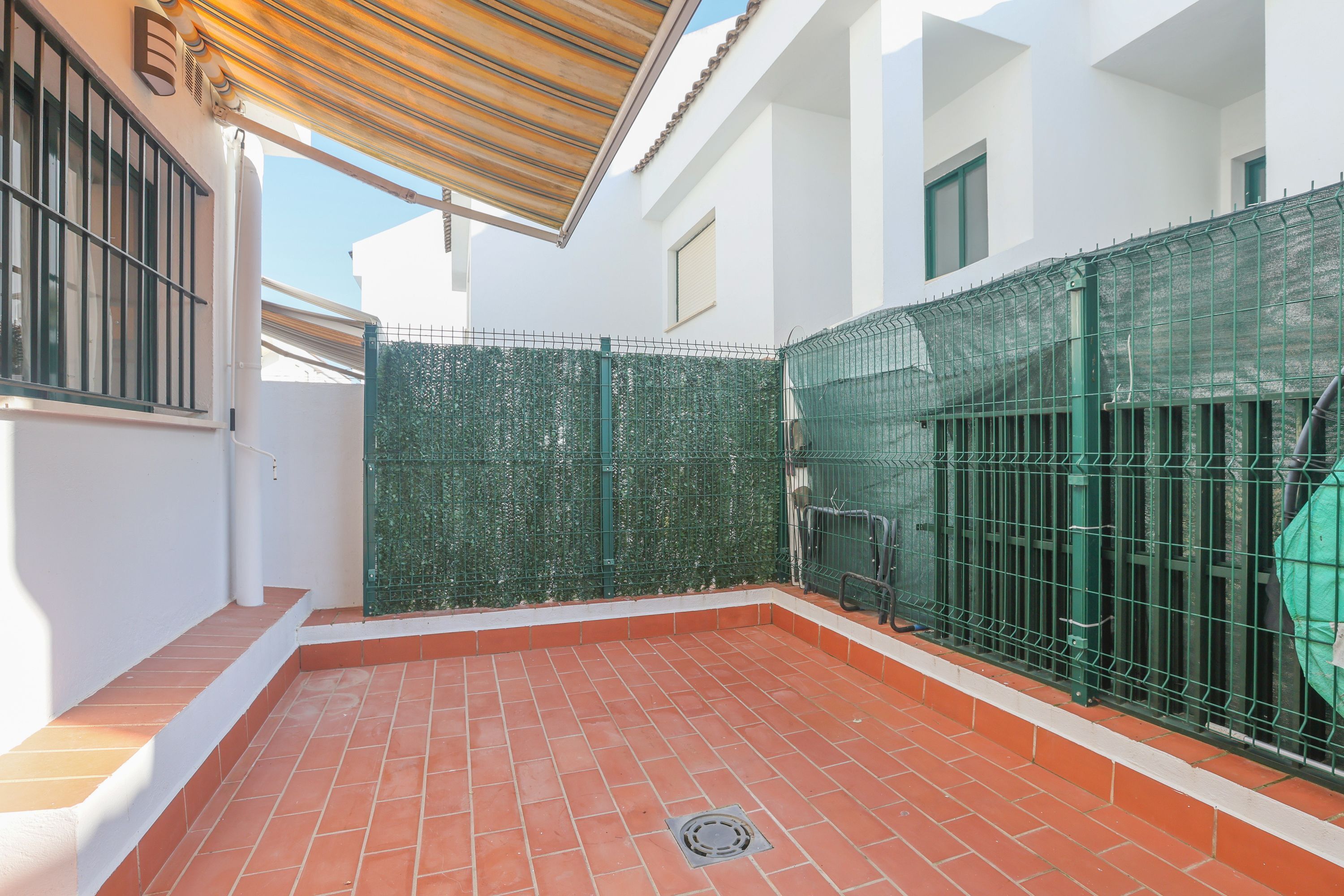 A courtyard with a tiled floor, a metal gate, and a wooden pergola.
