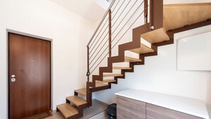 Un escalier moderne avec des marches en bois et des rampes en métal, menant à un mur blanc orné d’un miroir.
