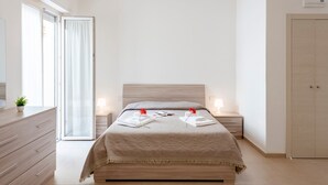 Une chambre à coucher moderne avec un lit, des tables de chevet, une commode et une porte-fenêtre coulissante.