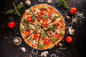A pizza with slices cut, surrounded by garlic, tomatoes, and basil leaves on a dark surface. - Teleo 82 50m Ski In - Ski Out 50m (Sestriere)