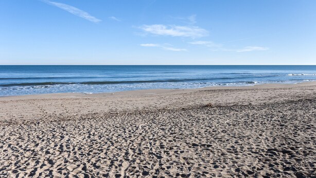 A sandy beach with footprints leading to the water, a clear sky, and gentle waves. - Sea Pearl in Daim s (Daimuz)