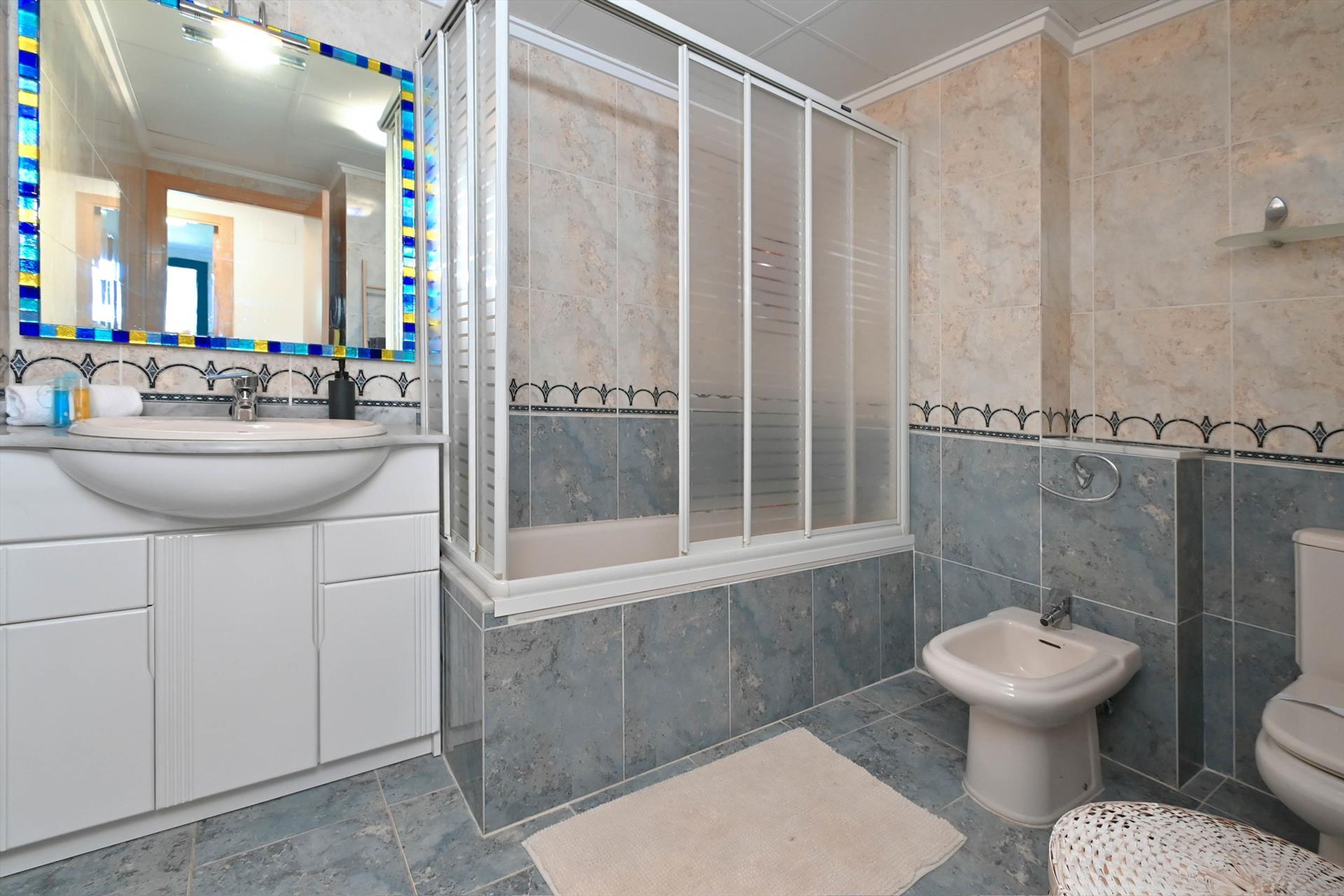 A modern bathroom with a large mirror, a shower enclosure, a bidet, and a sink.