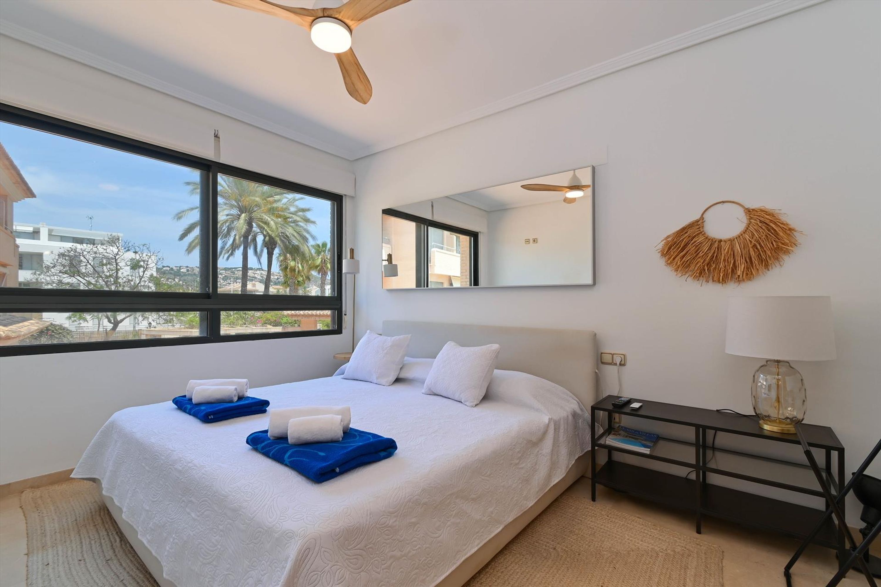 Une chambre d’hôtel moderne dotée d’un grand lit, d’un bureau, d’une chaise, d’un miroir et offrant une vue sur des palmiers.