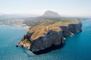 An aerial view of a coastal area with rocky cliffs, a clear blue sea, and a distant mountain. - Avatar in Bah a de J vea (Javea)