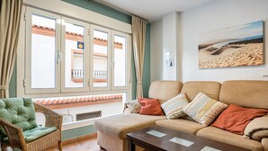Una sala de estar con un sofá, un sillón verde, una mesa de centro de madera y un ventanal con cortinas.